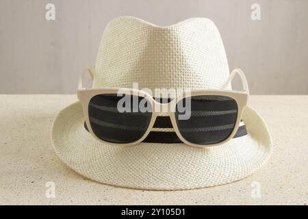 Strohhut mit Sonnenbrille mit weißem Rand auf dem Tisch, Vorderansicht des Hutes, Strandhut, mit Zubehör Stockfoto