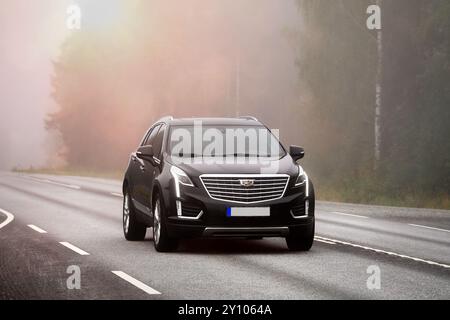 Schwarzes, modernes Cadillac-Auto mit Geschwindigkeit auf Highway 10 an einem nebeligen Morgen. Humppila, Finnland. August 2024. Stockfoto