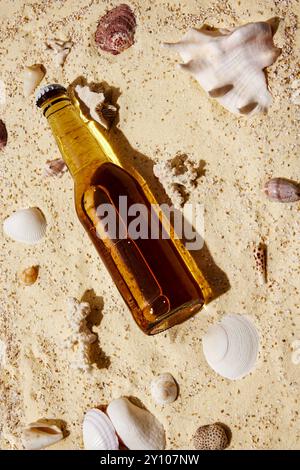 Eine Glasflasche liegt am Sandstrand, umgeben von Muscheln, und bietet ein erfrischendes Getränk für den Sommerurlaub. Stockfoto