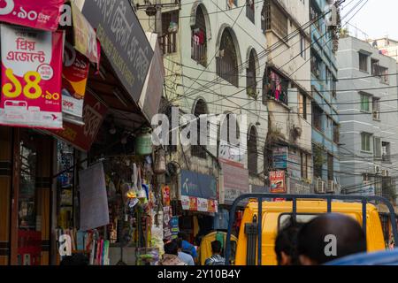 Dhaka, Bangladesch - 05.16.2023: Geschäftige Stadtstraße mit verworrenen Stromkabeln, mehrstöckigen Gebäuden und Geschäften. Schilder mit Text A Stockfoto