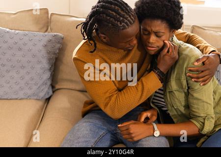 Tröstender Partner, afroamerikaner, der eine Frau auf der Couch zu Hause umarmt und tröstet Stockfoto