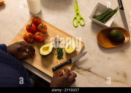 Zubereitung frischer Avocado und Tomaten auf Schneidebrett, afroamerikaner hackt Kräuter Stockfoto