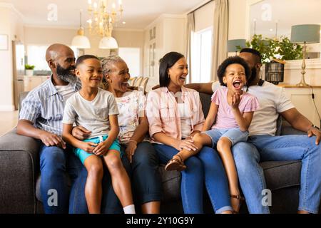 Lächelnde, generationsübergreifende Familie sitzt auf der Couch und genießt die gemeinsame Zeit zu Hause Stockfoto