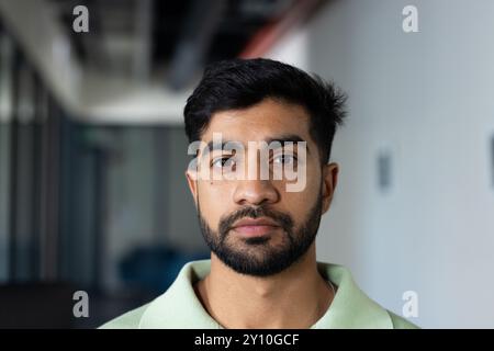 Indischer Mann im Amt, der mit ernstem Ausdruck in die Kamera schaut und ein grünes Hemd trägt Stockfoto