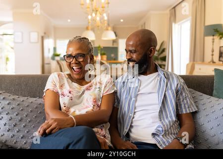 Lächelndes älteres Ehepaar, das auf der Couch sitzt und die Zeit zu Hause genießt Stockfoto
