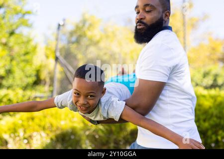 Draußen spielen, Vater hält den Sohn in Flugzeugposition, lächelnd und glücklich Stockfoto