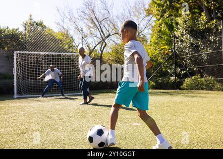 Fußball im Freien spielen, Junge mit dem Ball ins Tor treten, Großeltern und Enkel beobachten Stockfoto