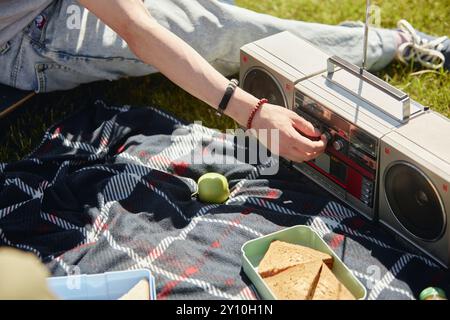 Nahaufnahme von Teenager-Jungs, die Band auf Vintage-Boombox drehen, während junge Freunde an sonnigen Tagen ein Picknick in der Natur genießen, Kopierraum Stockfoto