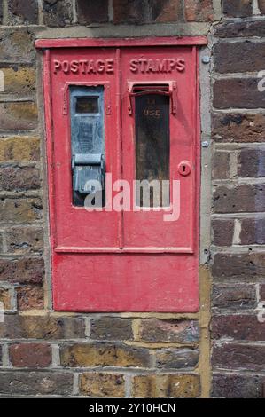 Der alte Münzautomat für Briefmarken, der in die Ziegelmauer eingebaut wurde, England, Großbritannien Stockfoto