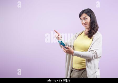 Eine Frau zeigt auf ein Handy. Sie sieht lächelnd in die Kamera aus. Stockfoto