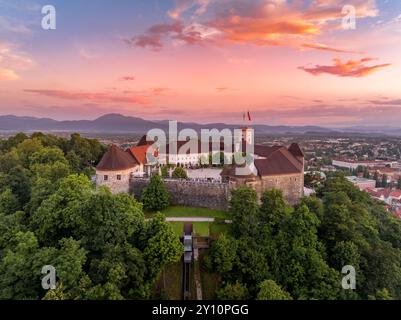 Blick auf die Burg von Ljubljana in Slowenien, Türme, Bastionen, Seilbahn, die Besucher den Hügel mit buntem Himmel hinauf bringt Stockfoto