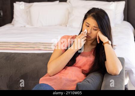 Sitzt auf der Couch, asiatische Frau wischt Tränen mit Taschentuch ab, fühlt sich traurig und emotional Stockfoto