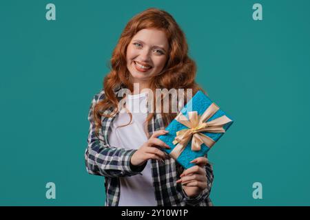 Glückliche junge Ingwerhaarige Frau mit Geschenkbox auf blauem Hintergrund. Positives Mädchen lächelt, in Händen. Bieten Sie Überraschung für Sie Stockfoto