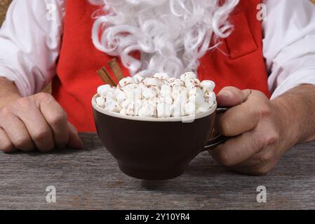 Nahaufnahme des Weihnachtsmanns, der einen Becher heißen heißen heißen heißen Kakao mit Marshmallows in der Hand hält. Stockfoto