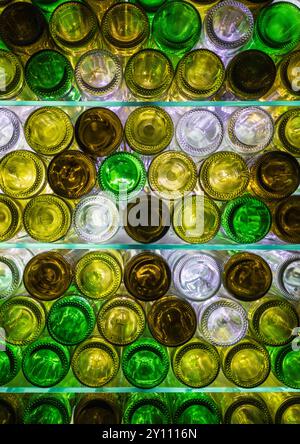 Natürlich beleuchtete, mehrfarbige Weinflaschen auf Glasregalen Stockfoto