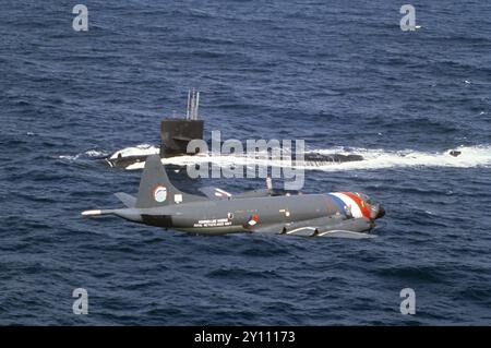 Ein Lockheed P-3 Orion Seefahrtflugzeug der Royal Dutch Navy fliegt während NATO-Übungen im Mittelmeer über einem US-U-Boot (März 1992) - UN aereo pattugliatore marittimo Lockheed P-3 Orion della Marina reale Olandese sorvola un sommergibile USA durante esercitazioni NATO in Mar Mediterraneo (marzo 1992) Stockfoto