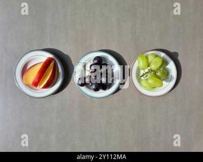 Frisches Obst auf einem weißen Teller, eine vitaminreiche Ernährung, gesunde frische helle und dunkle Trauben und geschnittene rote Apfel Stockfoto
