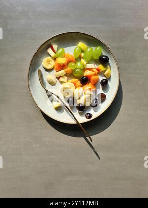 Frisches Obst auf einem weißen Teller, vitaminreiche Ernährung, gesundes frisches Obst als Obstsalat oder Snack mit Gabel Stockfoto