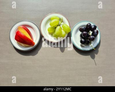 Frisches Obst auf einem weißen Teller, eine vitaminreiche Ernährung, gesunde frische helle und dunkle Trauben und geschnittene rote Apfel Stockfoto