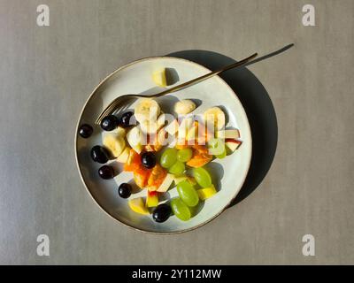 Frisches Obst auf einem weißen Teller, vitaminreiche Ernährung, gesundes frisches Obst als Obstsalat oder Snack mit Gabel Stockfoto