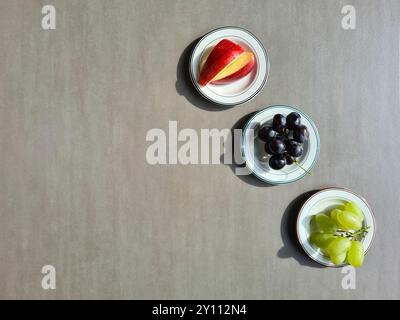 Frisches Obst auf einem weißen Teller, eine vitaminreiche Ernährung, gesunde frische helle und dunkle Trauben und geschnittene rote Apfel Stockfoto