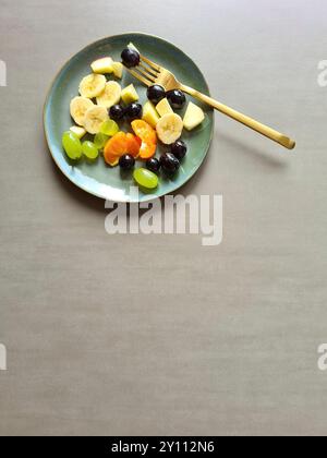 Frisches Obst auf weißem grünem Teller, vitaminreiche Ernährung, gesunde frische verschiedene Obstsorten serviert als Obstsalat oder Snack mit goldener Gabel Stockfoto