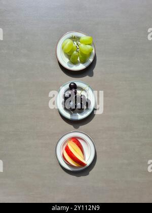 Frisches Obst auf einem weißen Teller, eine vitaminreiche Ernährung, gesunde frische helle und dunkle Trauben und geschnittene rote Apfel Stockfoto