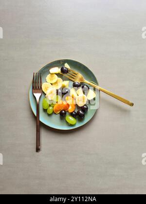 Frisches Obst auf blaugrünem Teller, vitaminreiche Ernährung, gesunde frische verschiedene Obstsorten als Obstsalat oder Snack mit zwei verschiedenen Gabeln Stockfoto