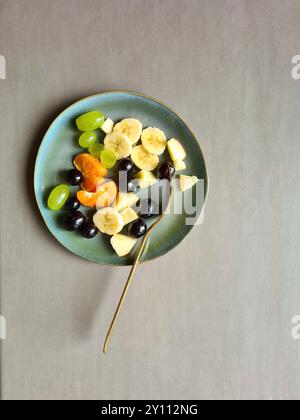 Frisches Obst auf weißem grünem Teller, vitaminreiche Ernährung, gesunde frische verschiedene Obstsorten serviert als Obstsalat oder Snack mit goldener Gabel Stockfoto