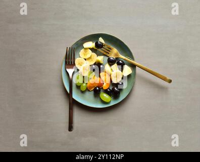 Frisches Obst auf grünem Teller, vitaminreiche Ernährung, gesundes frisches Obst als Obstsalat zwischendurch oder als Snack mit zwei Gabeln Stockfoto