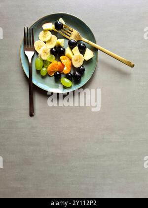Frisches Obst auf blaugrünem Teller, vitaminreiche Ernährung, gesunde frische verschiedene Obstsorten als Obstsalat oder Snack mit zwei verschiedenen Gabeln Stockfoto