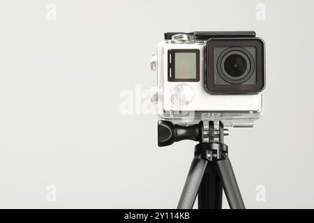 Moderne Action-Kamera und Stativ auf hellem Hintergrund. Leerzeichen für Text Stockfoto