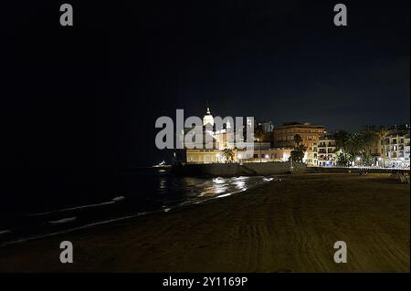 Sitges ruhige Nachtszene eines Strandes mit beleuchteten Gebäuden im Hintergrund, die ihr Licht auf dem Wasser reflektieren und die Ruhe und die Ruhe einfangen Stockfoto