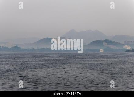 Künstlerische Architektur am unberührten See mit nebligem Berghintergrund am Morgen wird in Udaipur rajasthan india aufgenommen. Stockfoto