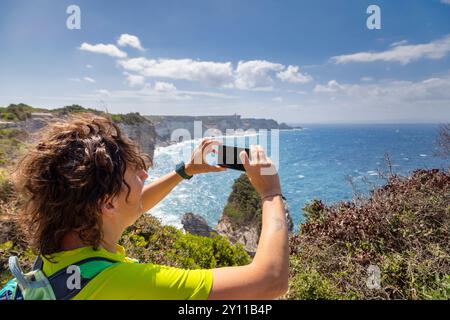 Weibliche Touristen fotografieren das Panorama der Straße von Bonifacio mit einem Smartphone, mit Cap Pertusato im Hintergrund. Bonifacio, Corse-du-Sud, Korsika, Frankreich Stockfoto