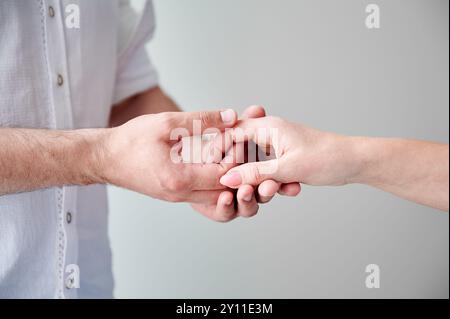 Nahaufnahme von zwei Händen, die eine zarte Berührung ausüben. Hände von Mann und Frau auf weißem neutralen Hintergrund. Der Mann hält die Hand seiner liebenswerten Frau. Konzept von Zuneigung, Unterstützung und gegenseitigem Respekt. Stockfoto