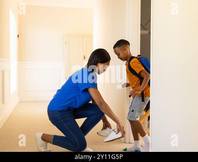 Ich helfe dem Kind, Schuhe anzuziehen, eine Frau, die den Jungen mit Rucksack für die Schule vorbereitet Stockfoto