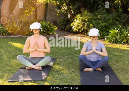 Yoga auf Matten üben, asiatische Großmutter und Enkelin mit vr-Headsets im Garten im Freien Stockfoto