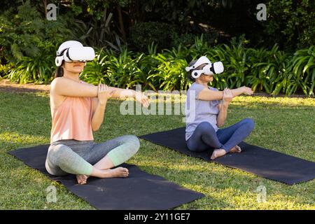 Mit VR-Headsets üben asiatische Großmutter und Enkelin Yoga auf Matten im Garten im Freien Stockfoto