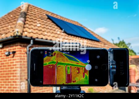 Eine Infrarot-Thermografie, die zur Beurteilung des Wärmeverlustes eines Bungalows mit Solarpaneelen auf dem Dach verwendet wird. Stockfoto