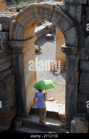 Ephesus, Türkei. Frau mit grünem Regenschirm, die durch eine gewölbte Passage in der antiken griechischen Stadt Ephesus geht. Stockfoto