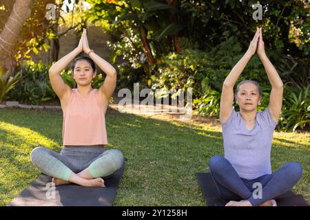 Yoga üben, asiatische Großmutter und Enkelin sitzen auf Matten im Garten und meditieren zusammen Stockfoto