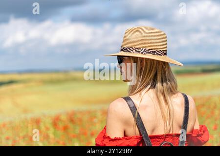 Junge blonde Frau in Sonnenbrille und Strohhut auf einem Feld mit rotem Mohn Stockfoto