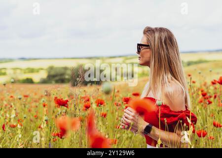 Junge blonde Frau in Sonnenbrille mit rotem Mohn in den Händen auf einem Mohnfeld Stockfoto