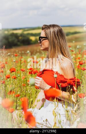 Junge blonde Frau in Sonnenbrille mit rotem Mohn in den Händen auf einem Mohnfeld Stockfoto