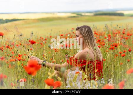 Blonde Frau pflückt Blumen auf einem Feld mit rotem Mohn. Stockfoto