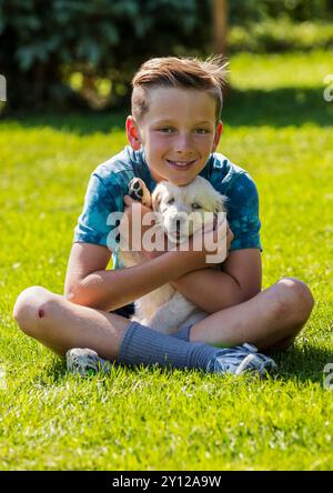 Junge, der mit einem platinfarbenen Golden Retriever Welpen auf einem Grasfeld spielt. Stockfoto