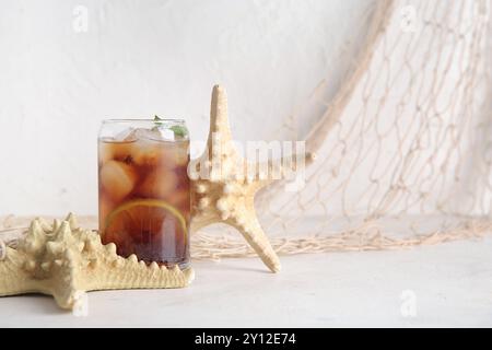 Ein Glas kalter Cuba Libre Cocktail und Seesterne auf weißem Hintergrund Stockfoto