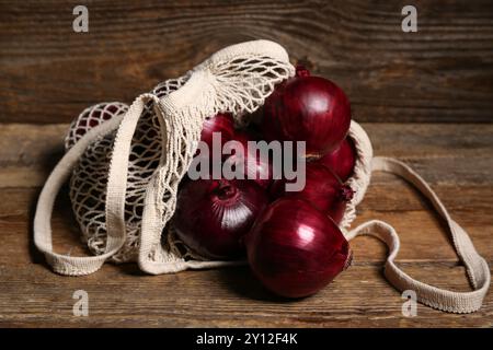 Schnur-Beutel mit frischen roten Zwiebeln auf hölzernem Hintergrund Stockfoto