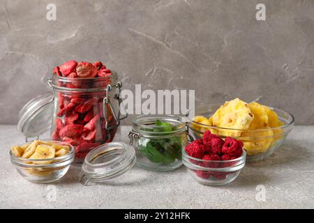 Glasschalen und Gläser mit verschiedenen getrockneten Früchten und Beeren auf grauem Hintergrund Stockfoto